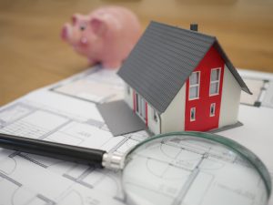 Model house, a magnifying glass, and a piggy bank on top of papers